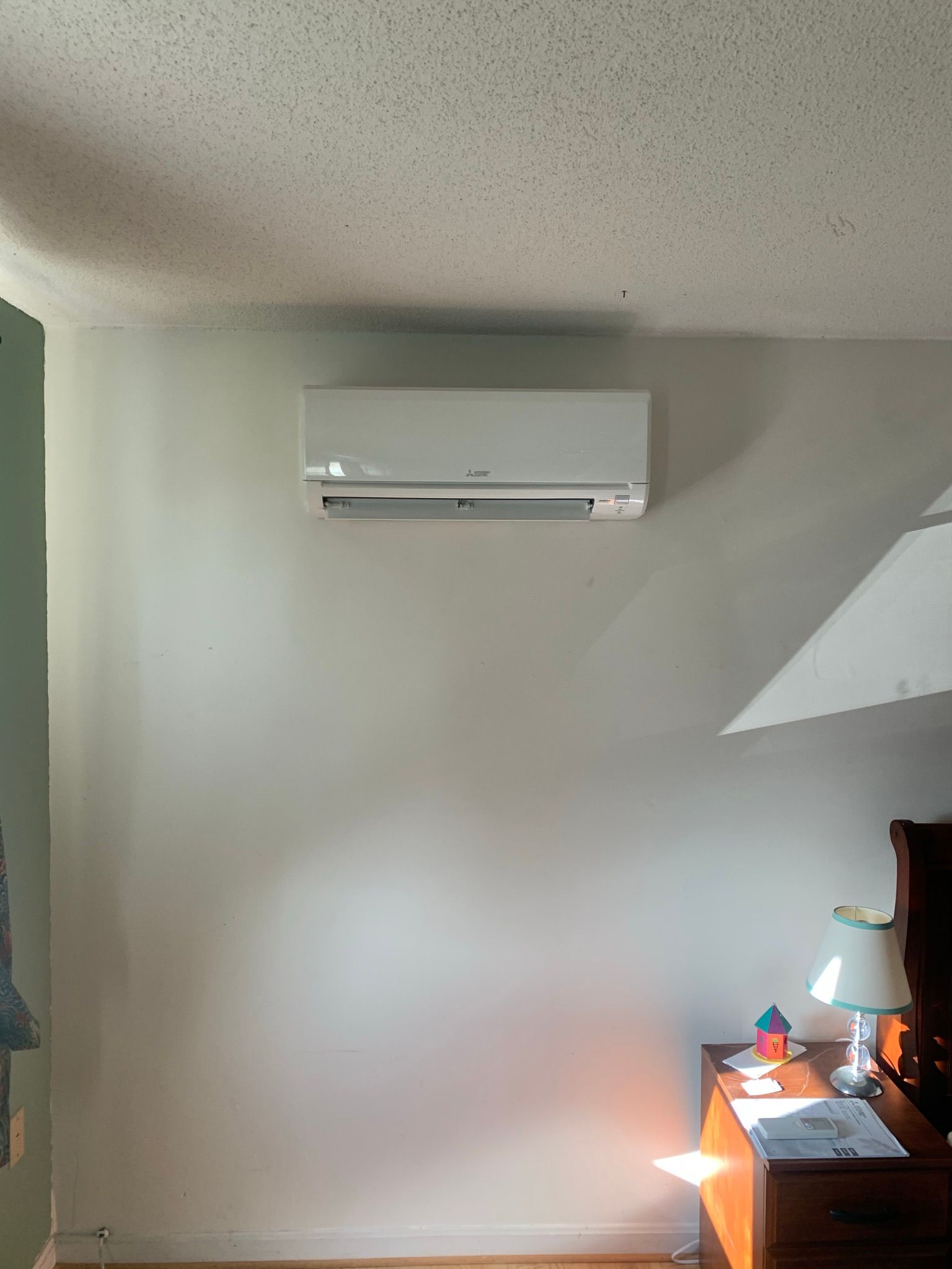 White wall-mounted air conditioner above a nightstand with a lamp.