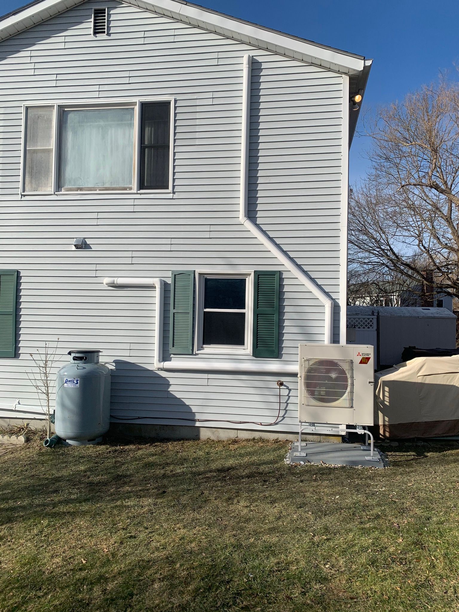 Side view of a white house with windows, shutters, a propane tank, and an outdoor AC unit.