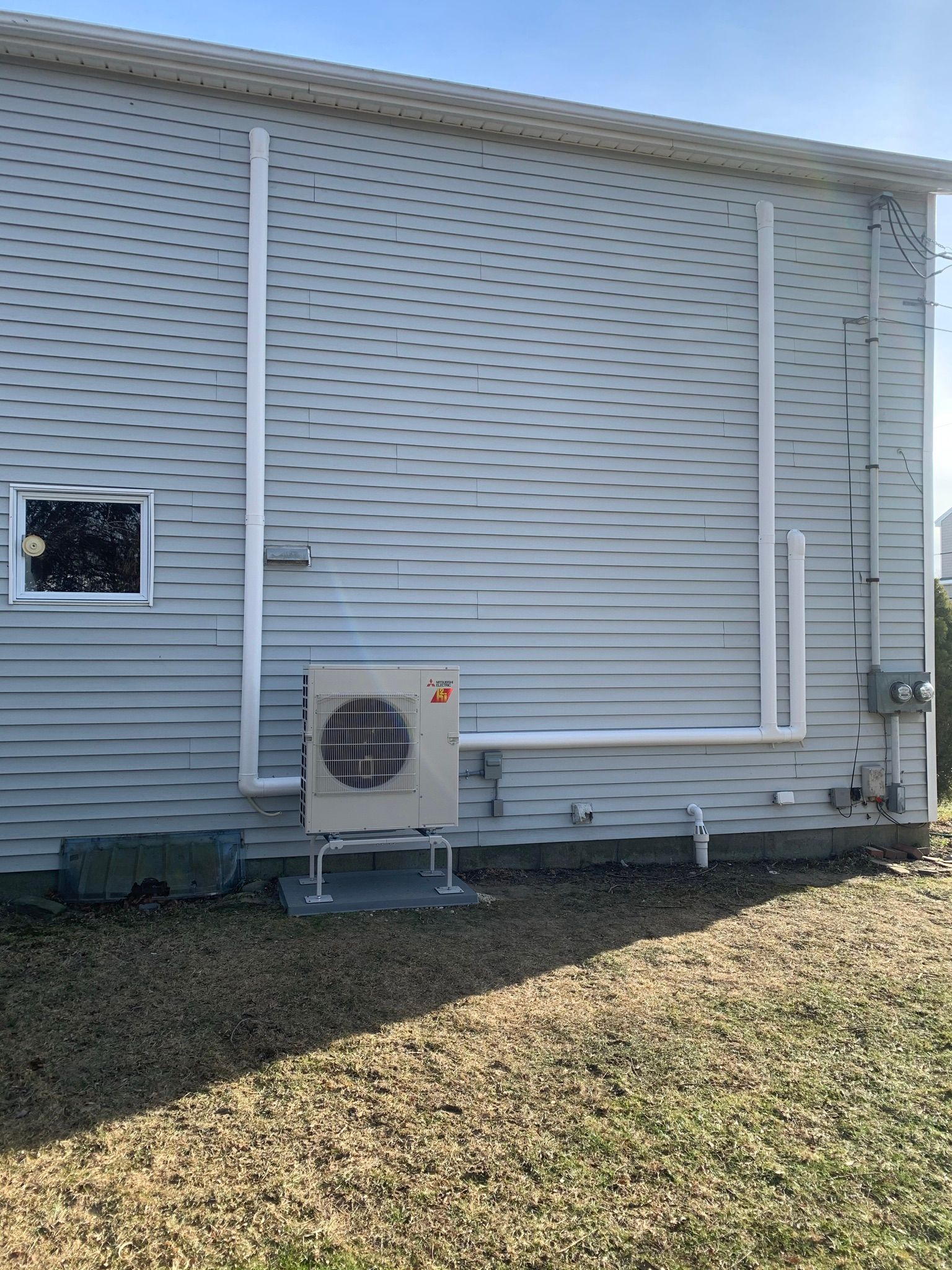 Exterior of a building with an AC unit and white pipes against gray siding.