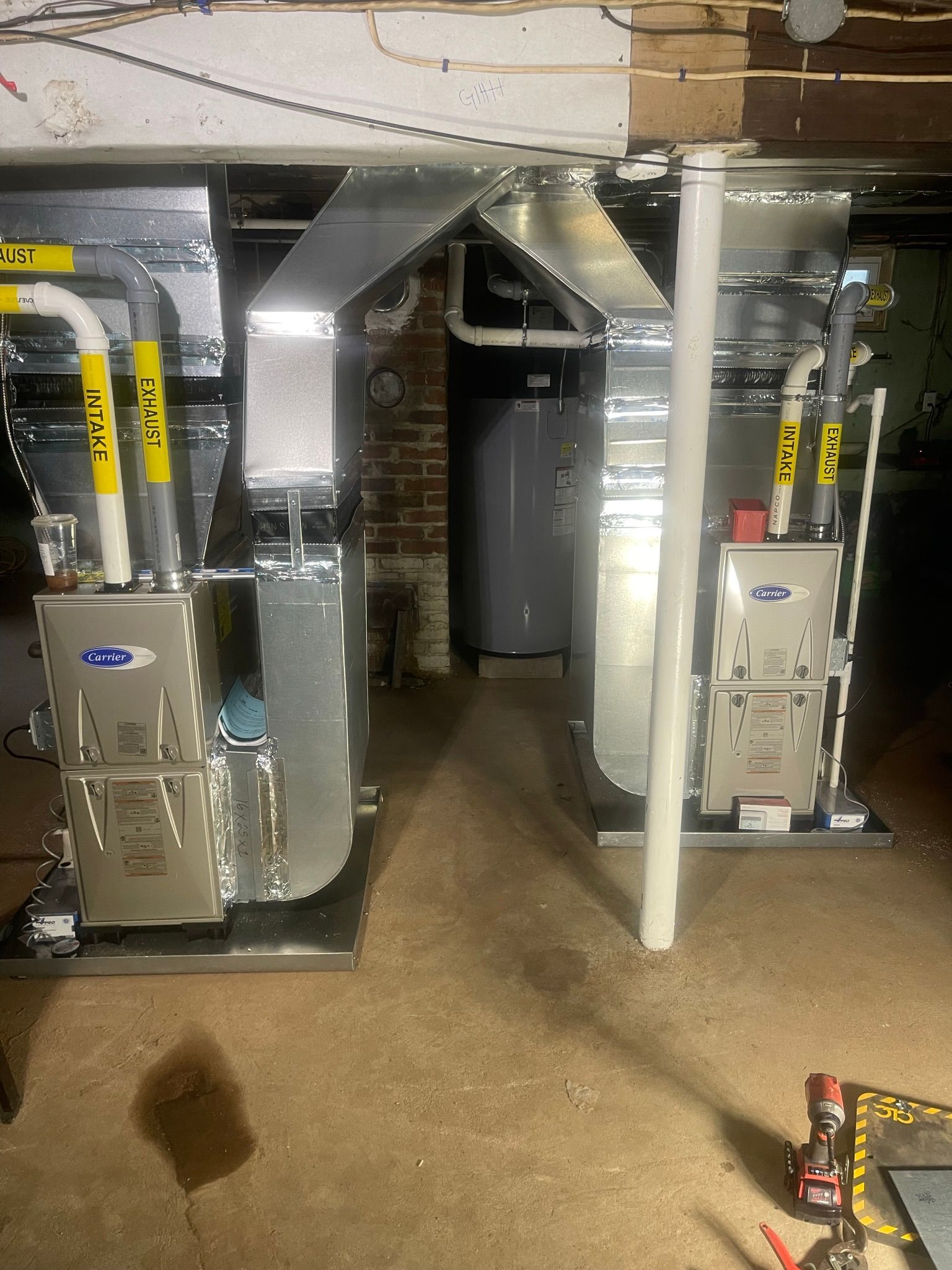 Two furnaces with ductwork in a basement setting. A water heater is visible in the background.