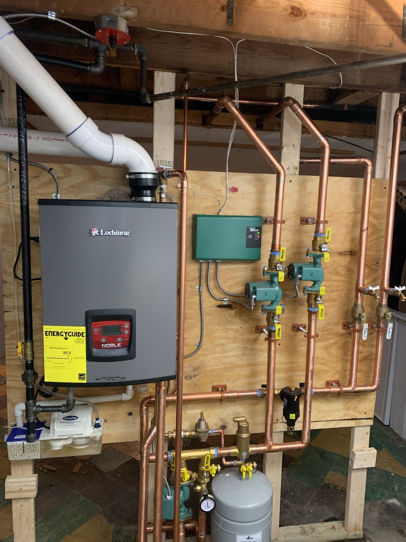 Copper pipes and water heater on a wooden wall in a basement.