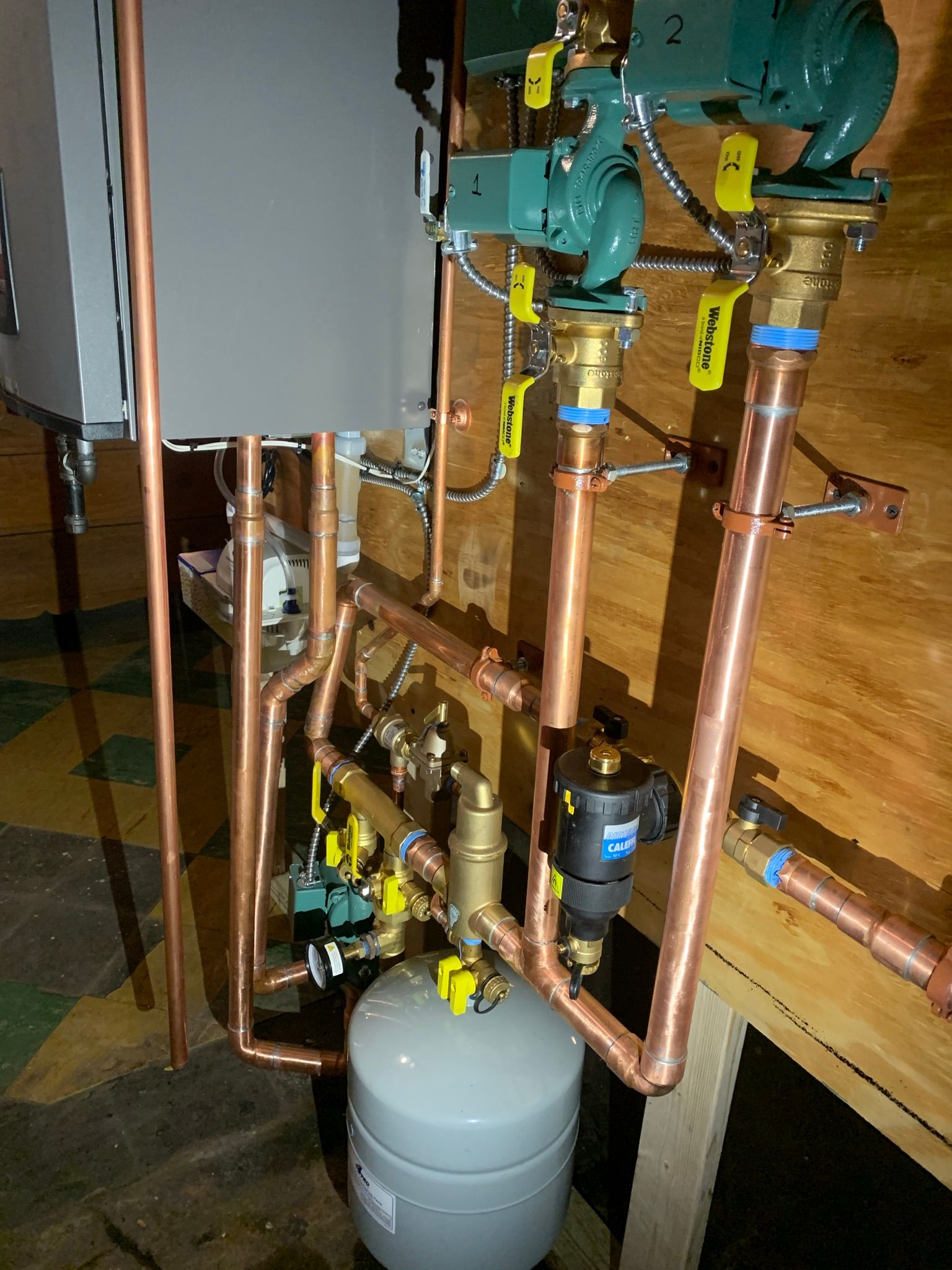Copper pipes and boiler system components on a wooden wall.