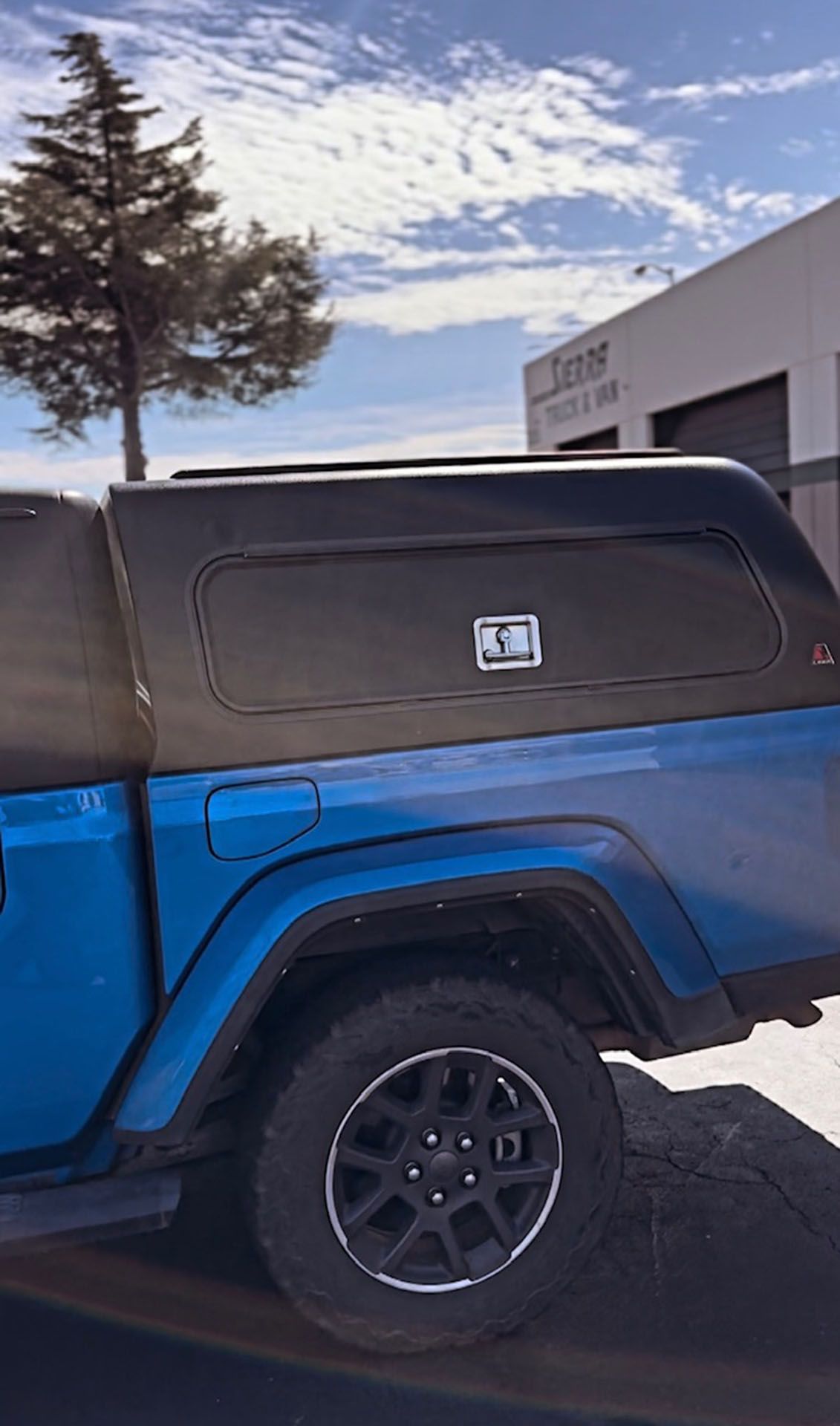 Blue off-road truck with black canopy parked beside a building on a snowy day