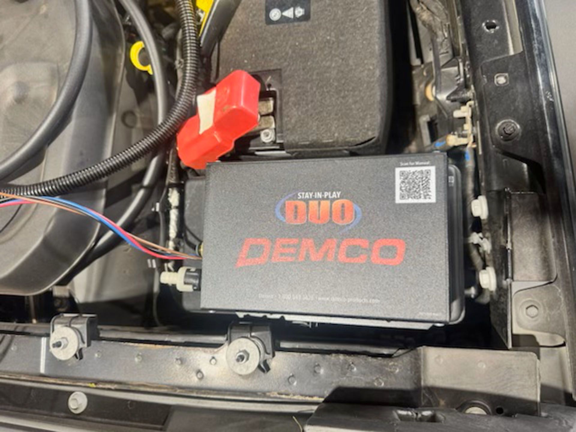 Black battery monitor module mounted inside a vehicle with red connector and wiring