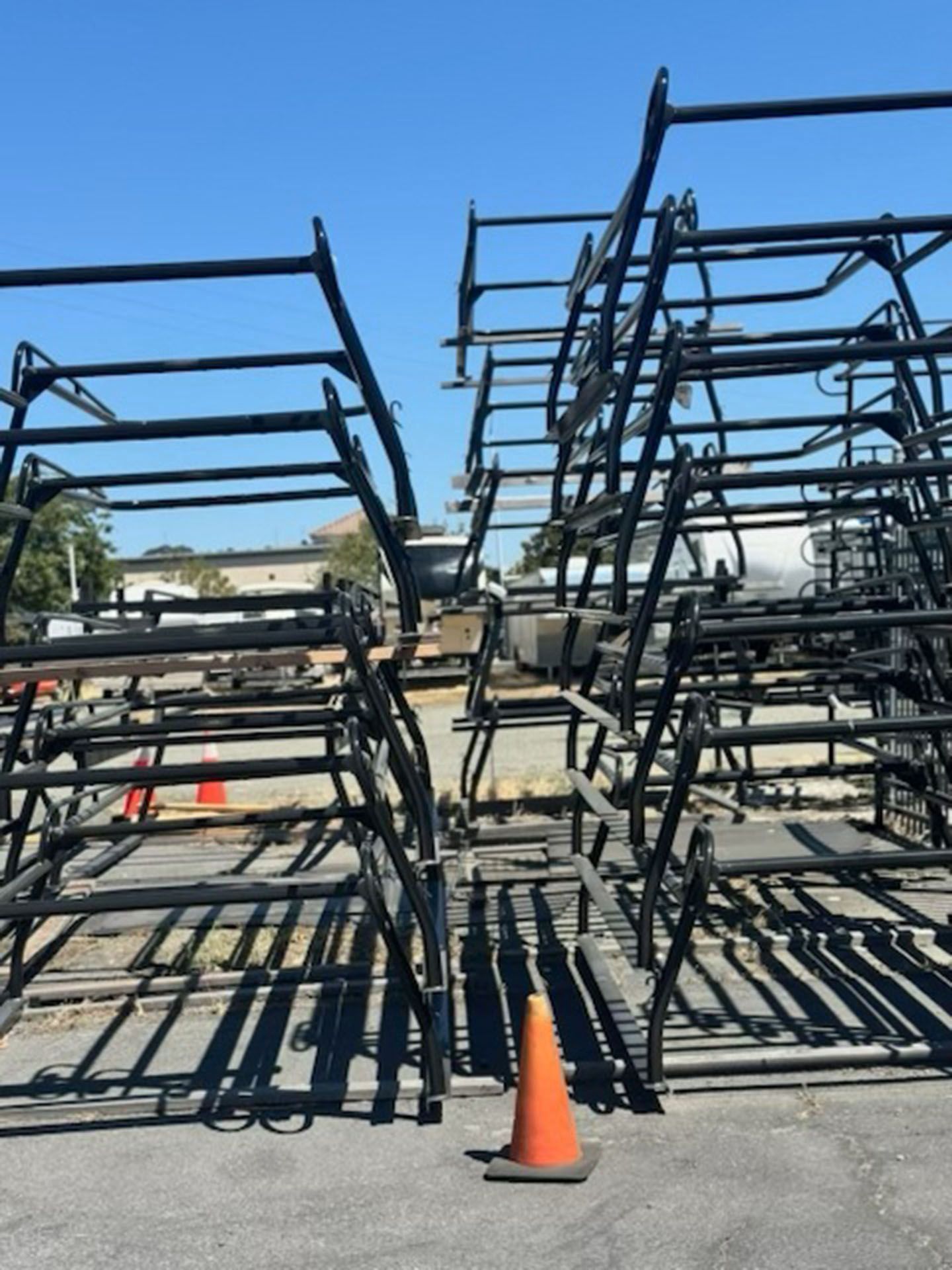 Stacks of black metal racks outdoors on asphalt, with an orange traffic cone in front