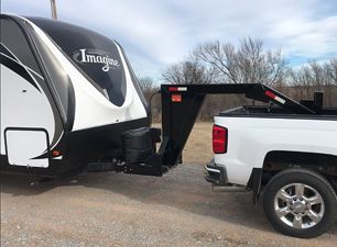 White pickup truck towing a black-and-white travel trailer on a gravel lot