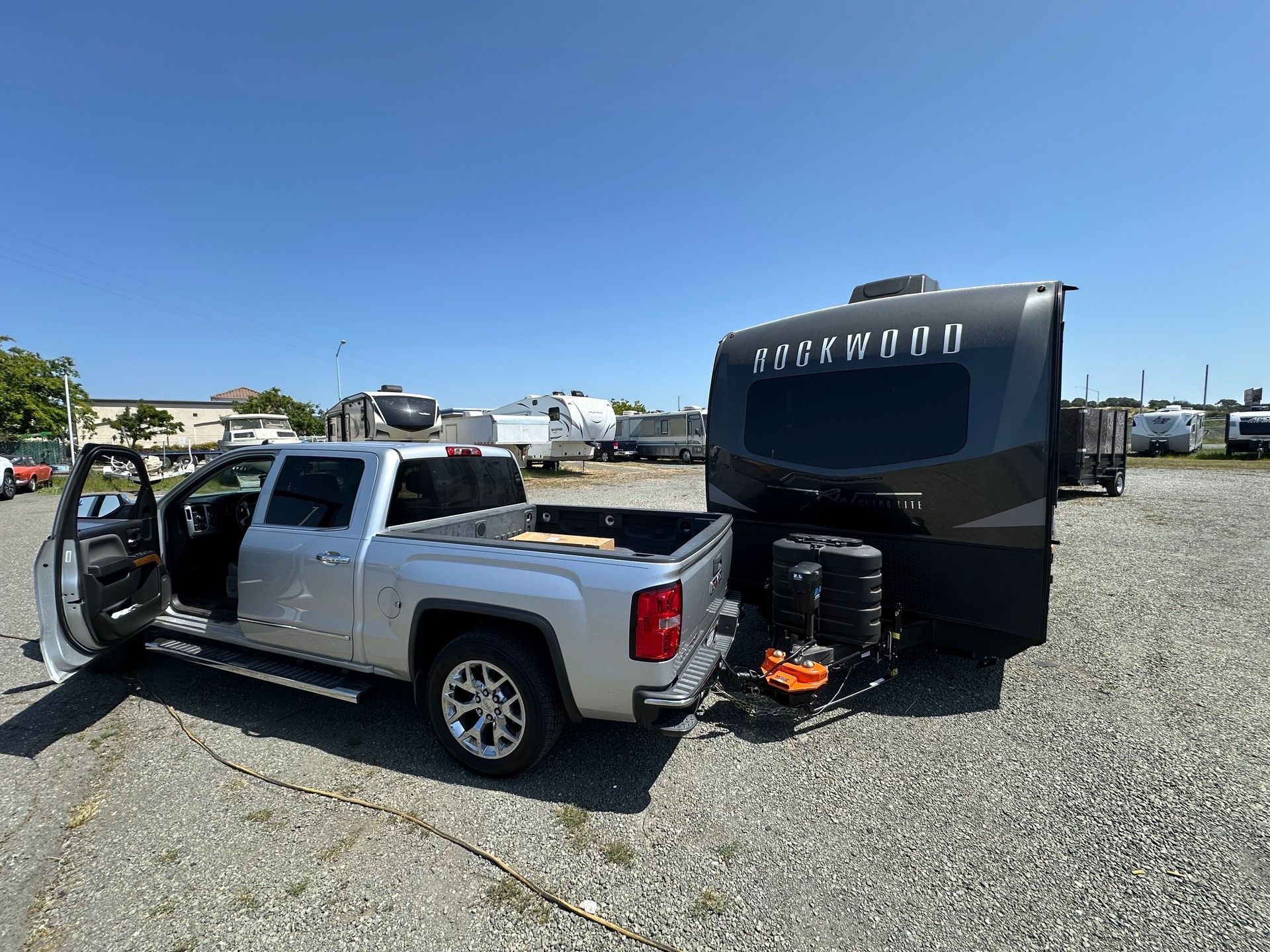 A silver truck is towing a trailer in a gravel lot.
