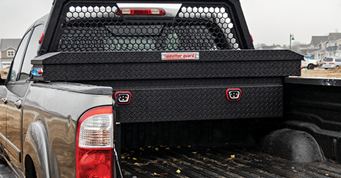 Black pickup truck with a toolbox in the bed and a rear window guard, parked outdoors.