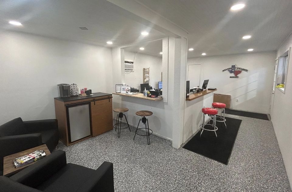 A waiting room with chairs, stools, a refrigerator and a counter.