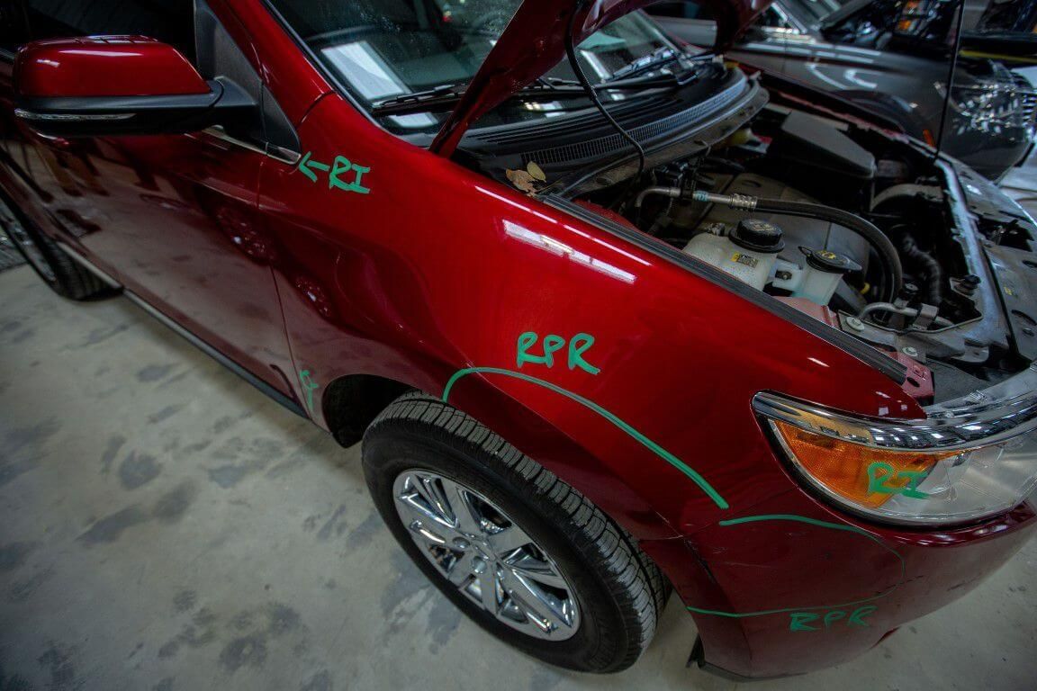 A red car with the hood open has rpr written on the side