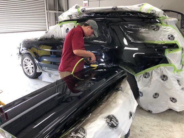 A man is polishing a black car in a garage.