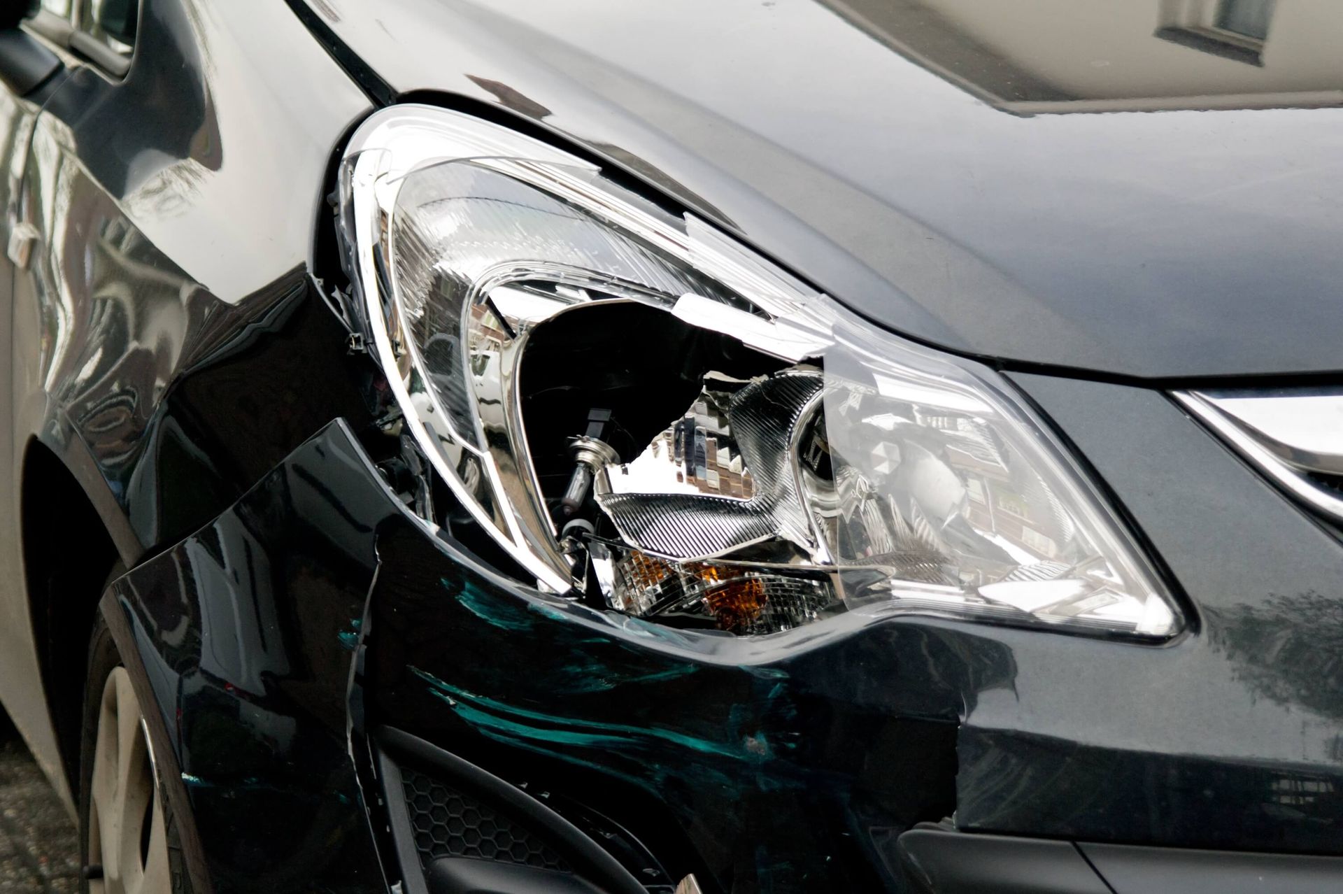 A close up of a black car with a broken headlight