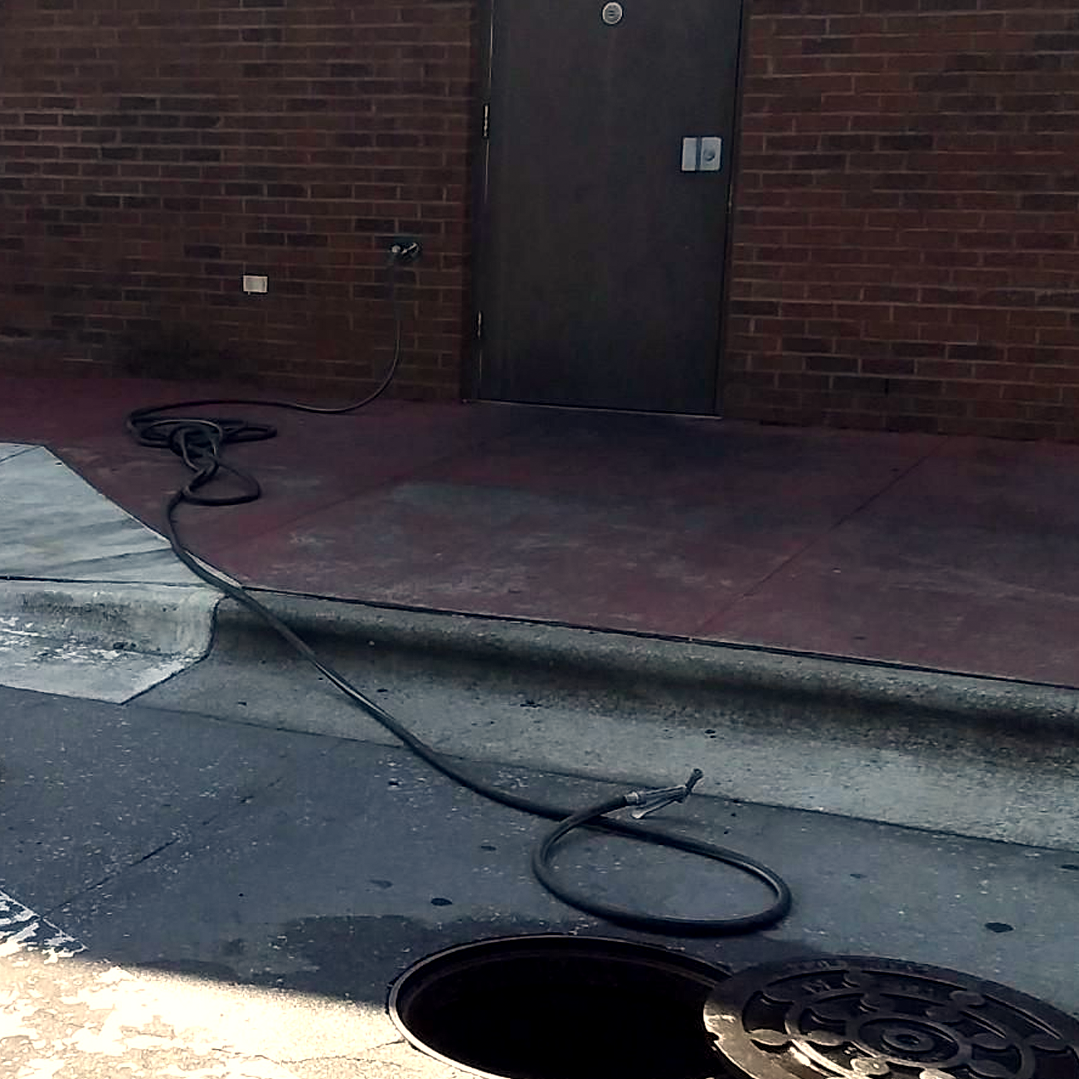 A hose is connected to a manhole cover on the side of the road.