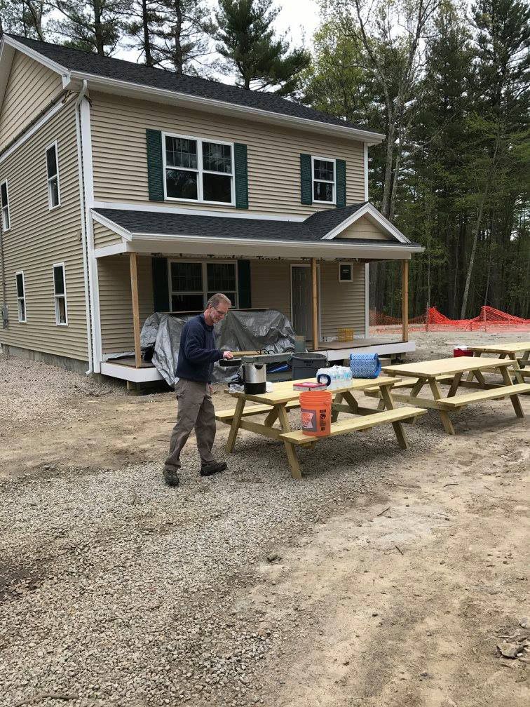 A man is standing in front of a house next to a picnic table.