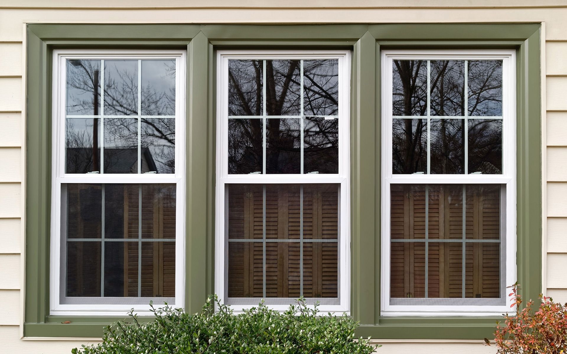 Three windows on a house with green trim and shutters