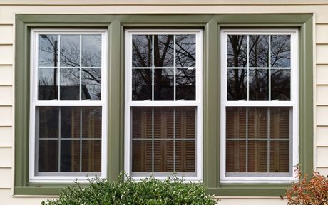 Three windows on a house with green trim and shutters