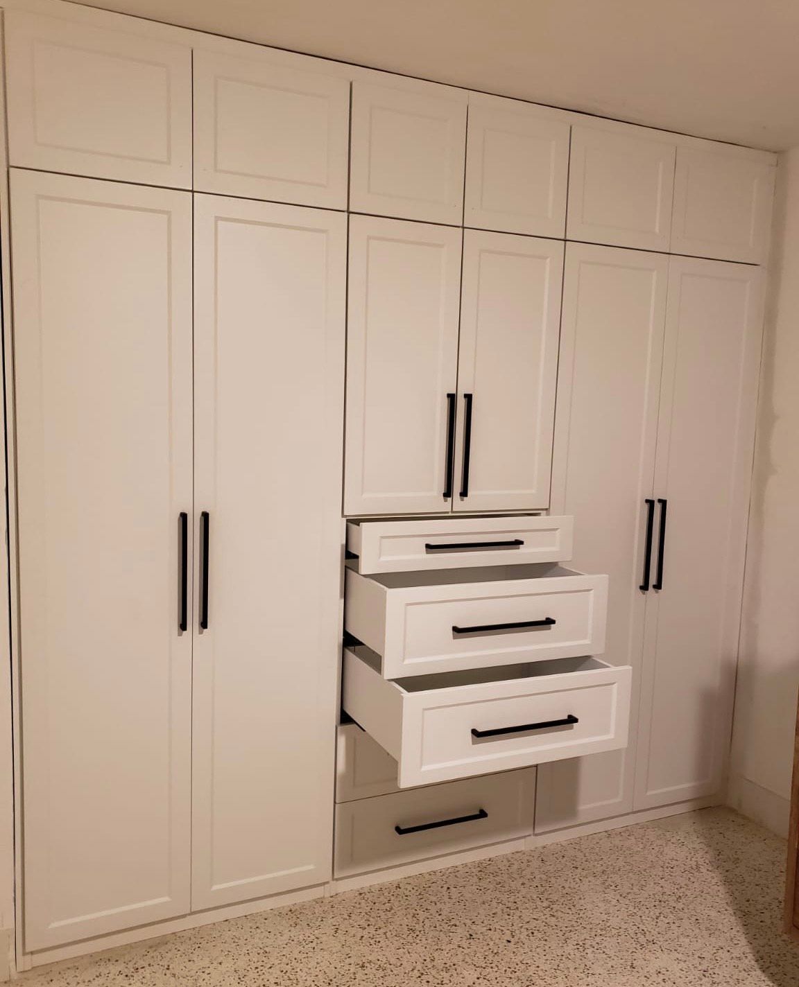 A room with a lot of white cabinets and drawers.