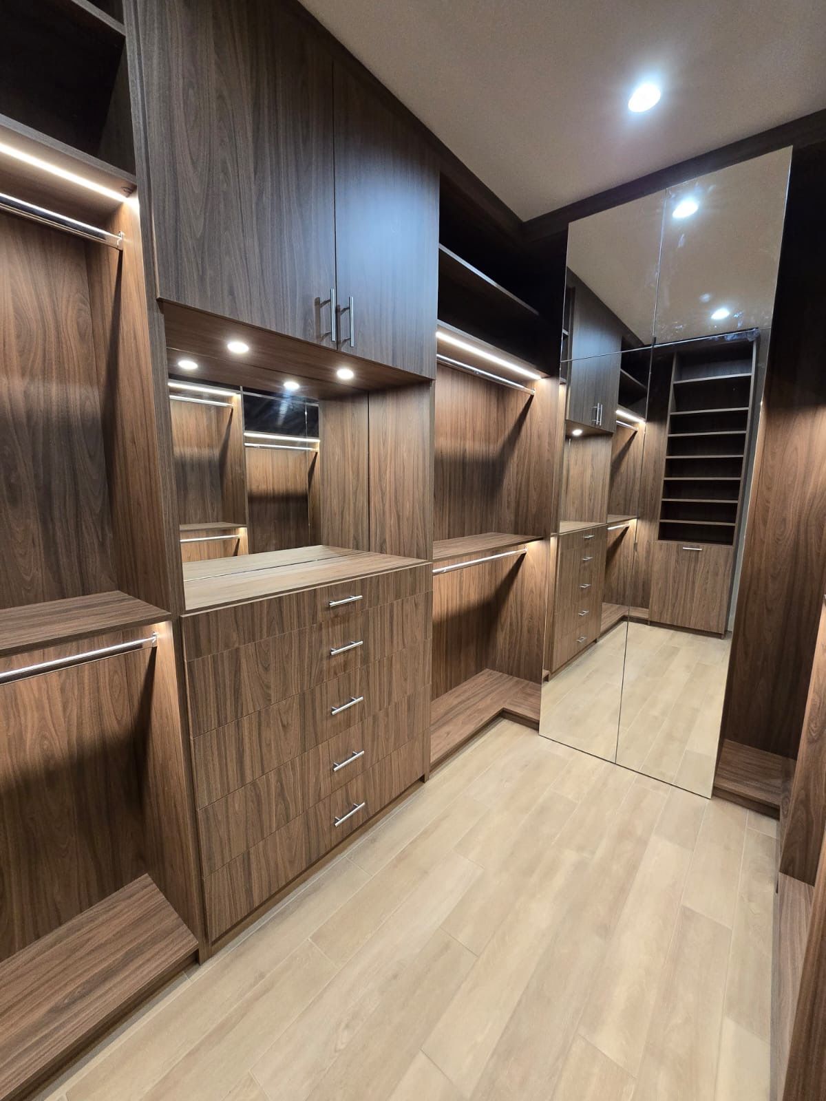 A walk in closet with wooden cabinets and a large mirror.