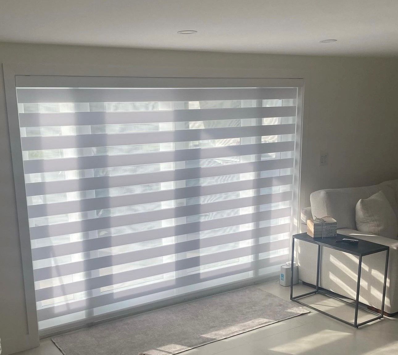 A living room with a couch, a table, and a large window with blinds on it.