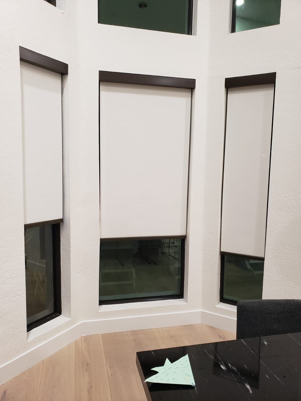 A living room with white blinds on the windows and a black table.