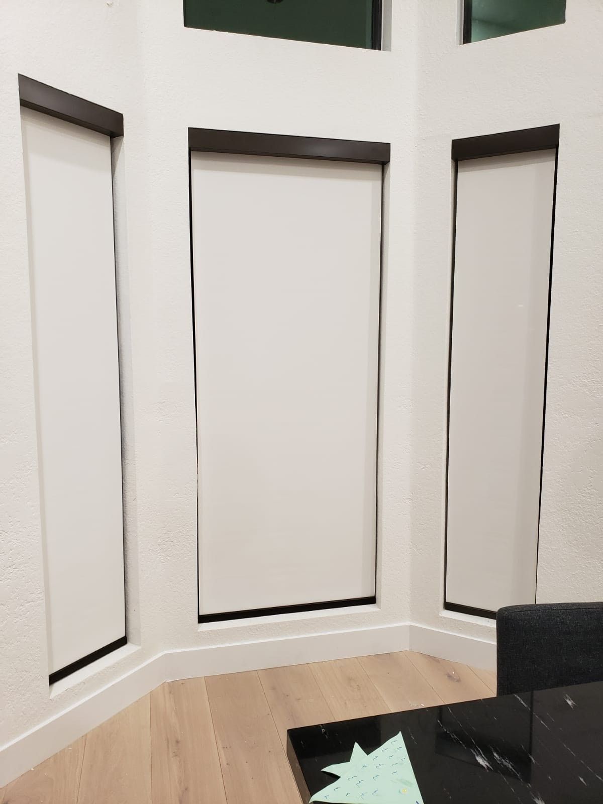 A living room with three windows and a black table.