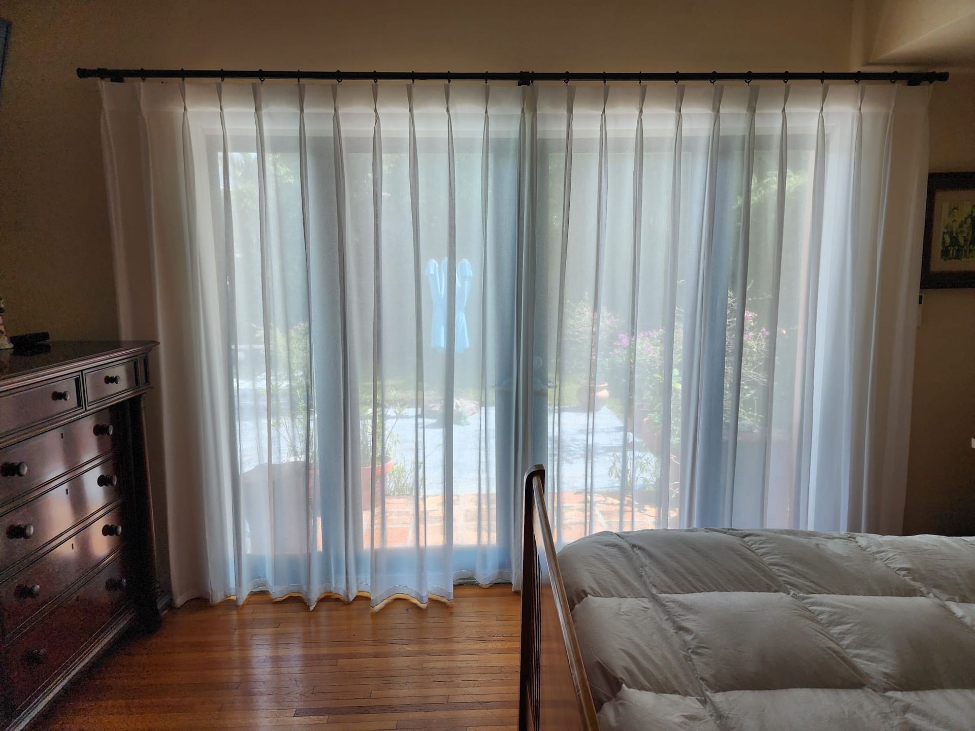 A bedroom with a bed and sliding glass doors with white curtains.