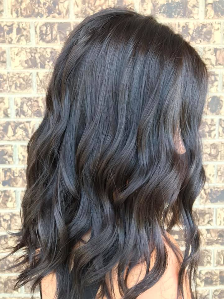 A woman with long dark hair is standing in front of a brick wall.