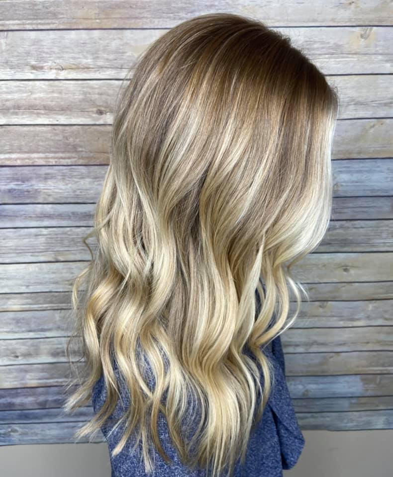 A woman with long blonde hair is standing in front of a wooden wall.