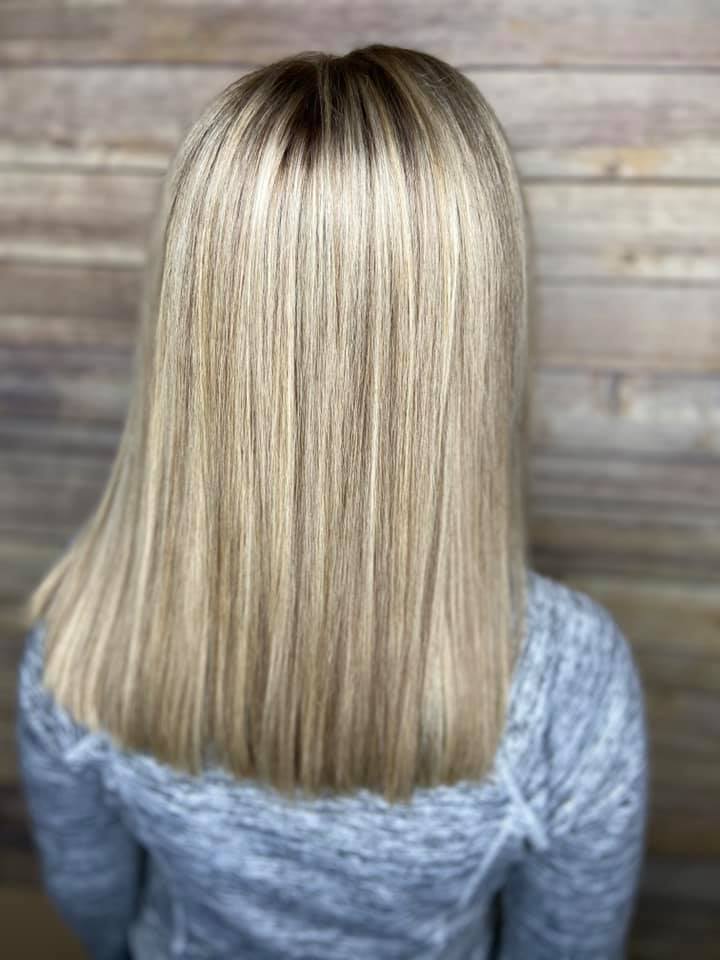 A woman with blonde hair is wearing a grey sweater and standing in front of a wooden wall.