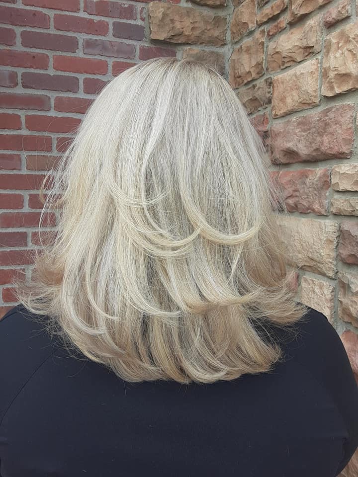 A woman with blonde hair is standing in front of a brick wall.