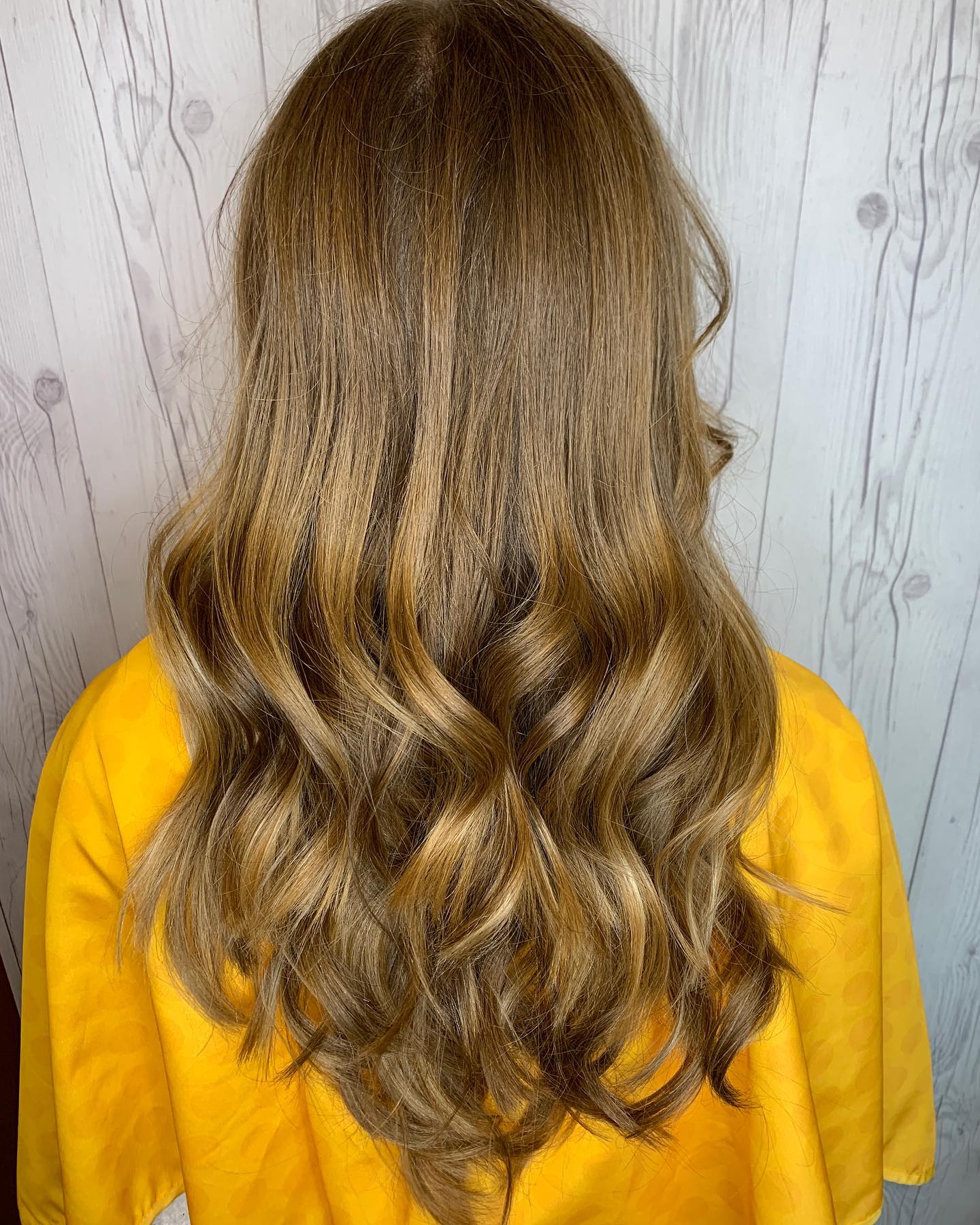 A woman with long wavy brown hair is wearing a yellow shirt.