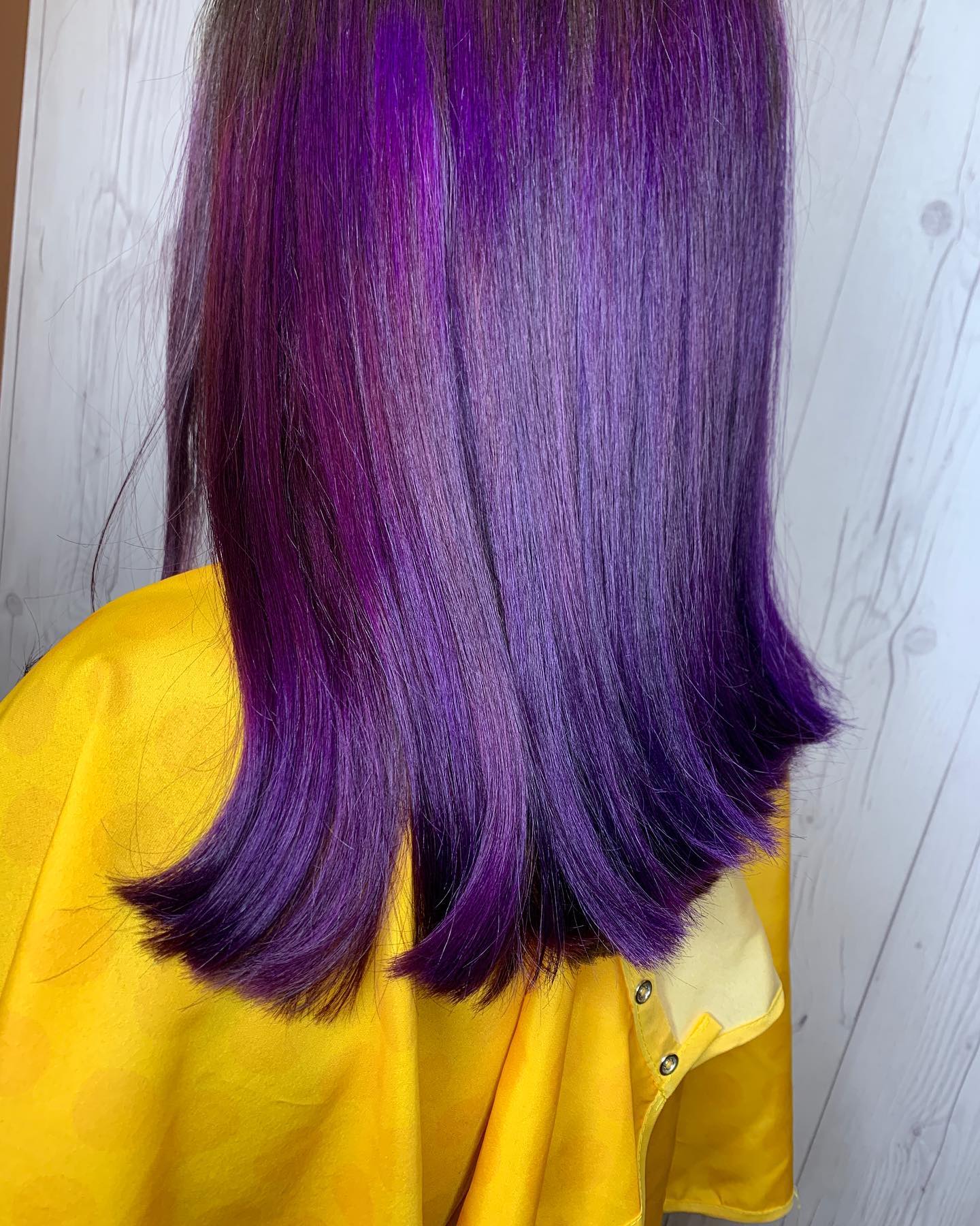 A woman with purple hair is wearing a yellow cape.