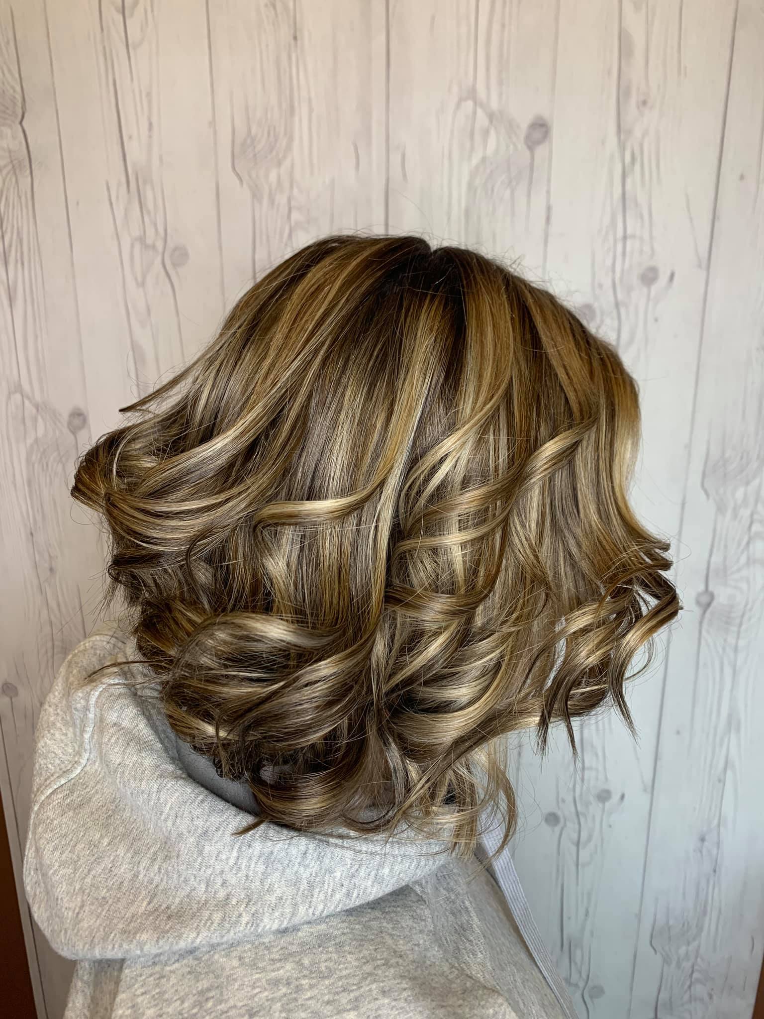 A woman wearing a wig is standing in front of a wooden wall.