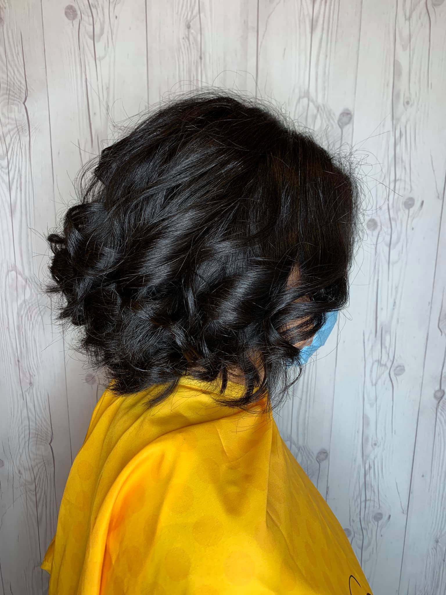 A woman wearing a yellow cape and a blue mask is standing in front of a wooden wall.