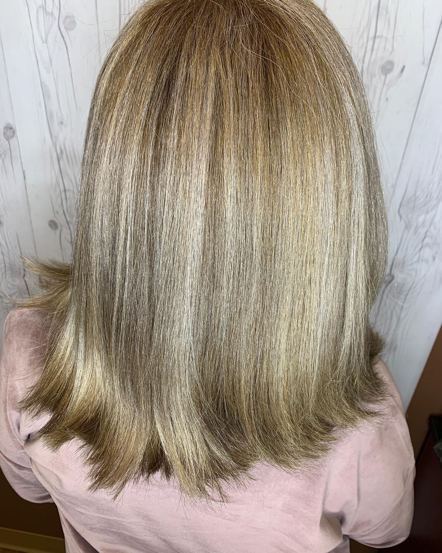 The back of a woman 's head with blonde hair and a pink shirt.