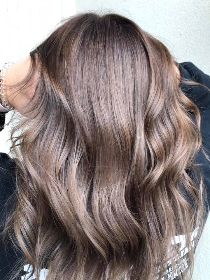 A woman with long wavy brown hair is wearing a black shirt.