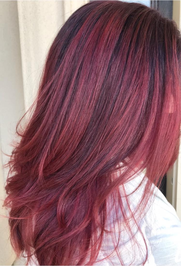 A woman with long red hair is standing in front of a window.