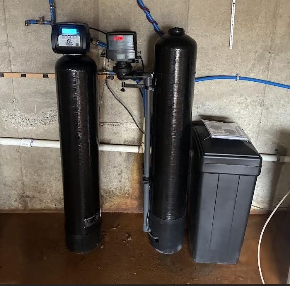 Water filtration and heater system in a basement setting. Tanks are various sizes and colors, with copper pipes.