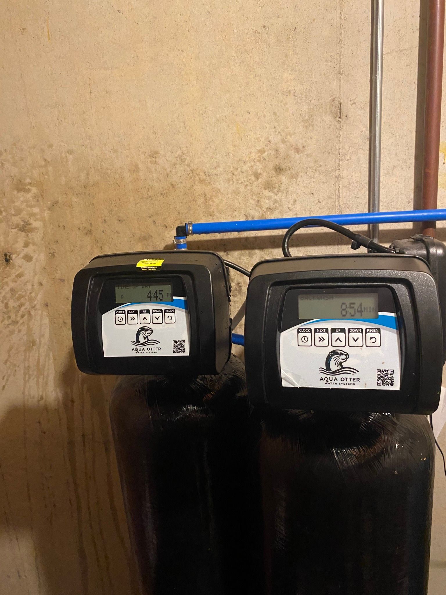 Two water filtration systems with digital displays against a concrete wall.