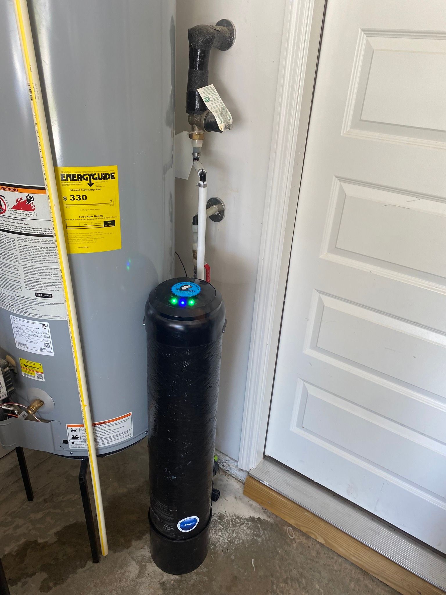 Water heater next to a black water softener, near a door.