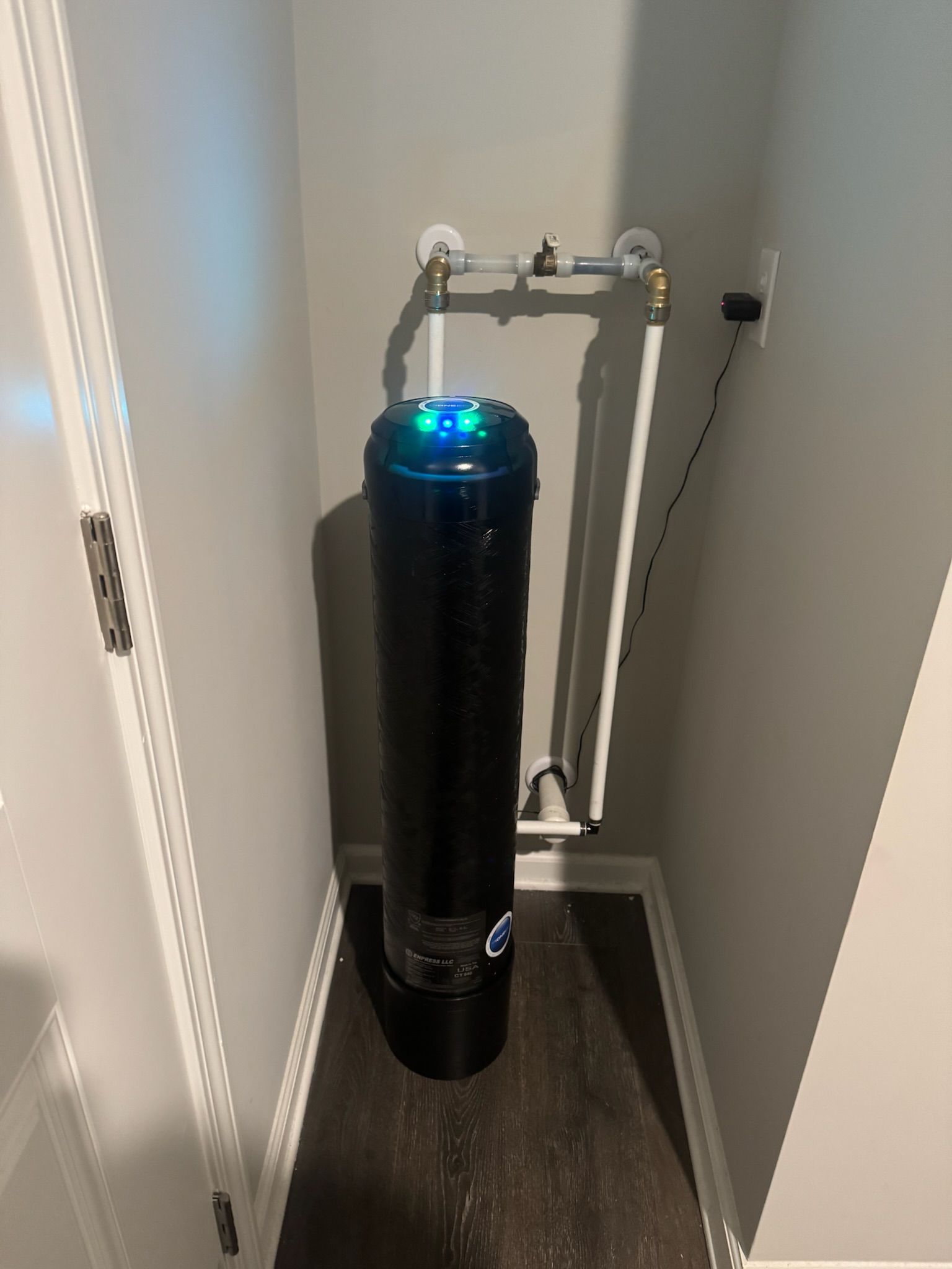 Black water filtration system in a small corner, connected to pipes. Blue light on top.