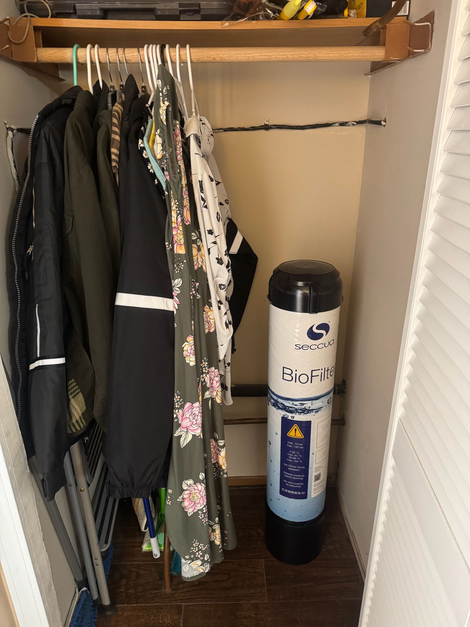 Clothes hanging in a closet with a water filter.