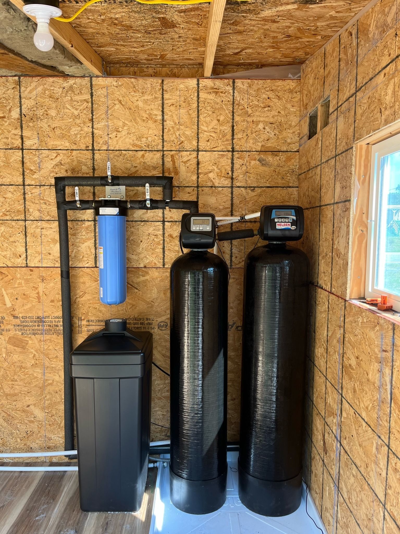 Water filtration system in a wooden shed. Includes filter, softener tanks, salt storage, and piping.