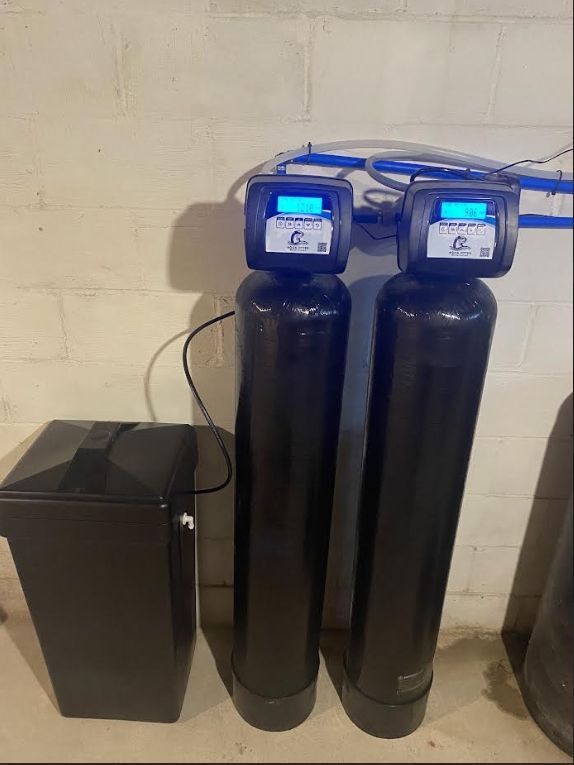 Water filtration system with two black tanks and a salt storage tank against a white wall.