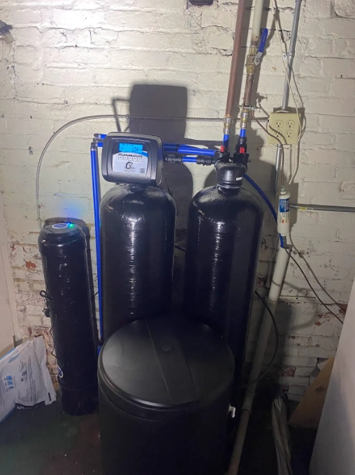 Water filtration system against a white brick wall; black tanks and blue pipes.