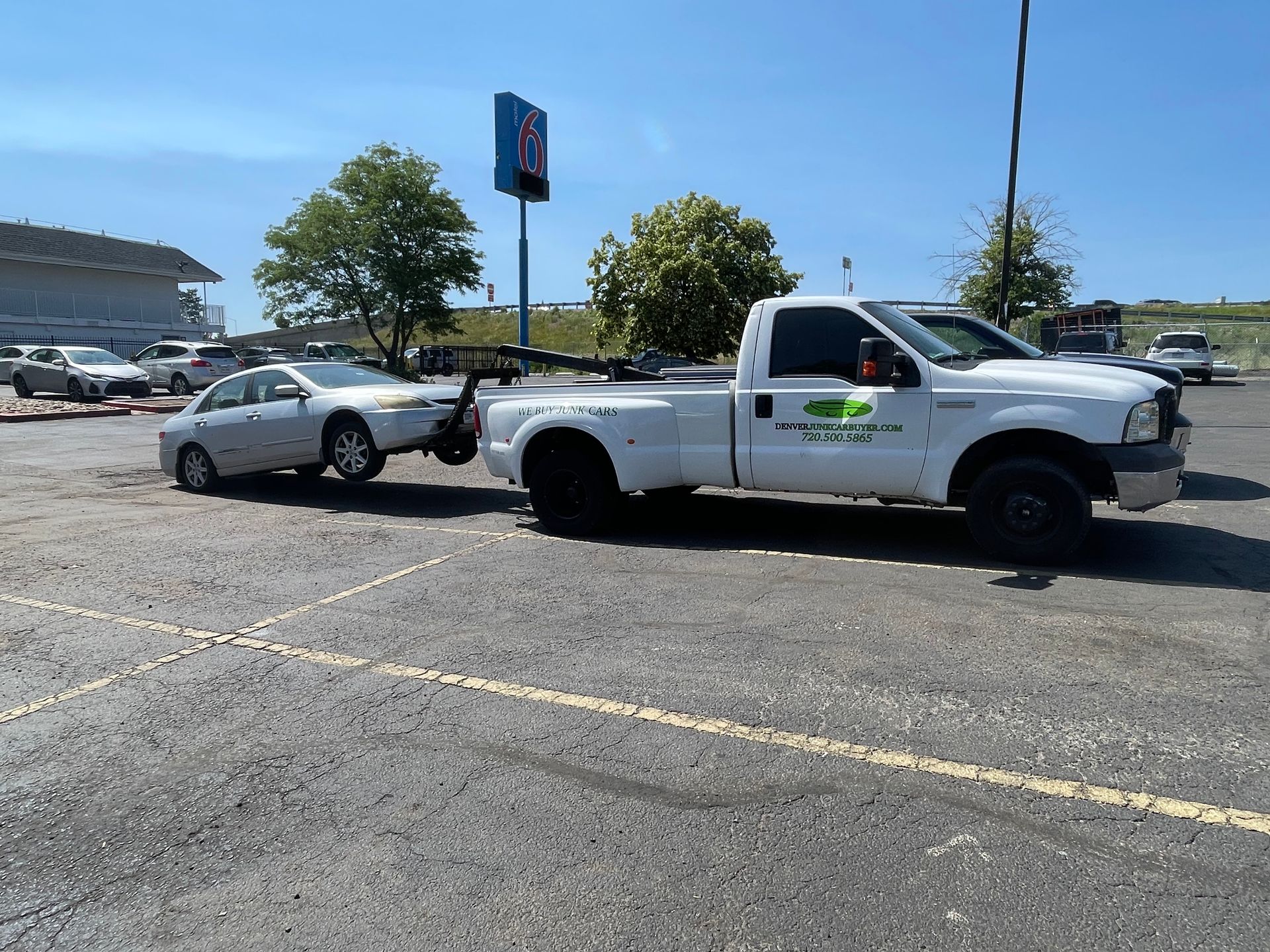 White tow truck hauling a silver car in a parking lot on a sunny day