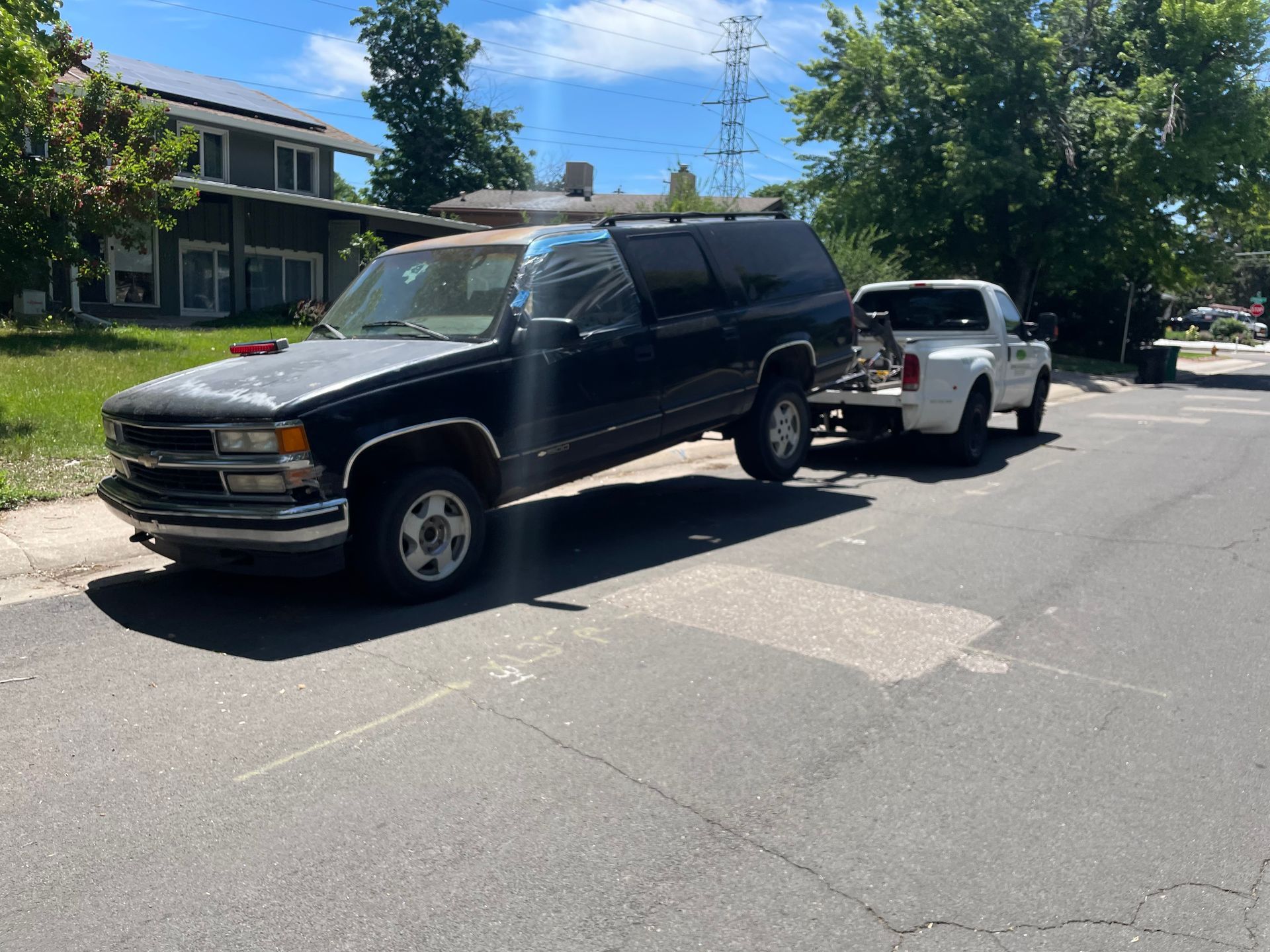 Black SUV towing a white car on a sunny residential street