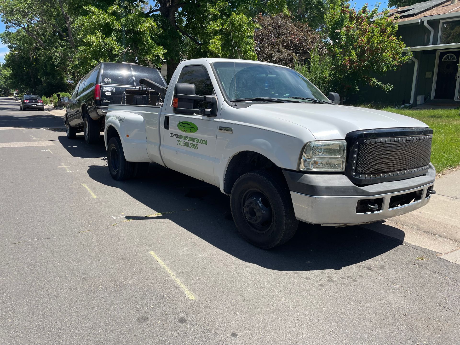 White pickup truck towing a black SUV on a sunny residential street