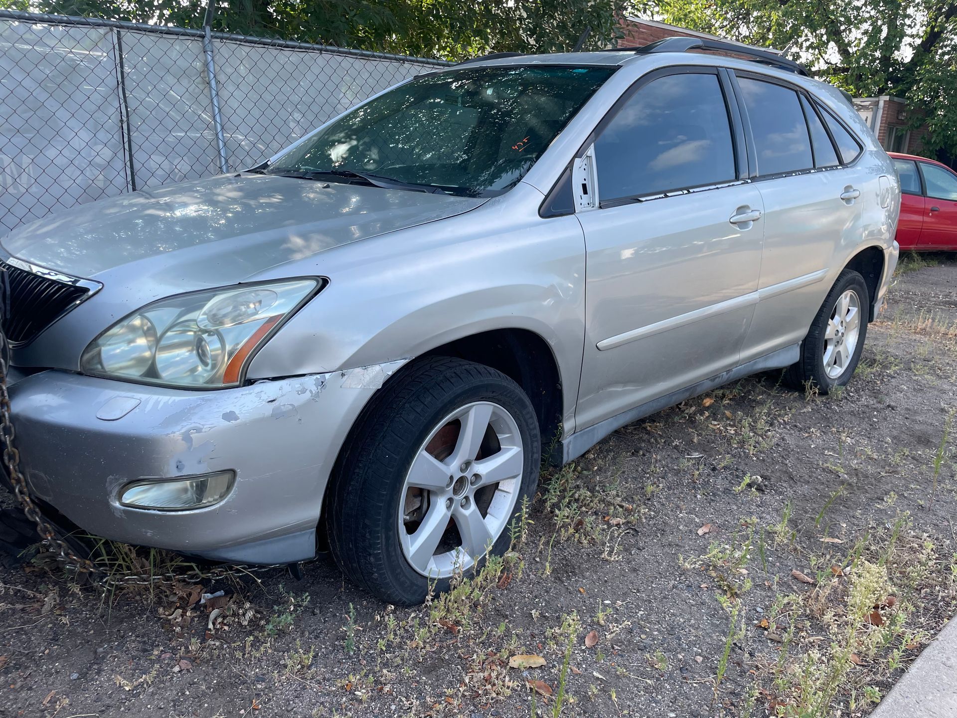 Silver sedan parked on gravel beside a chain-link fence