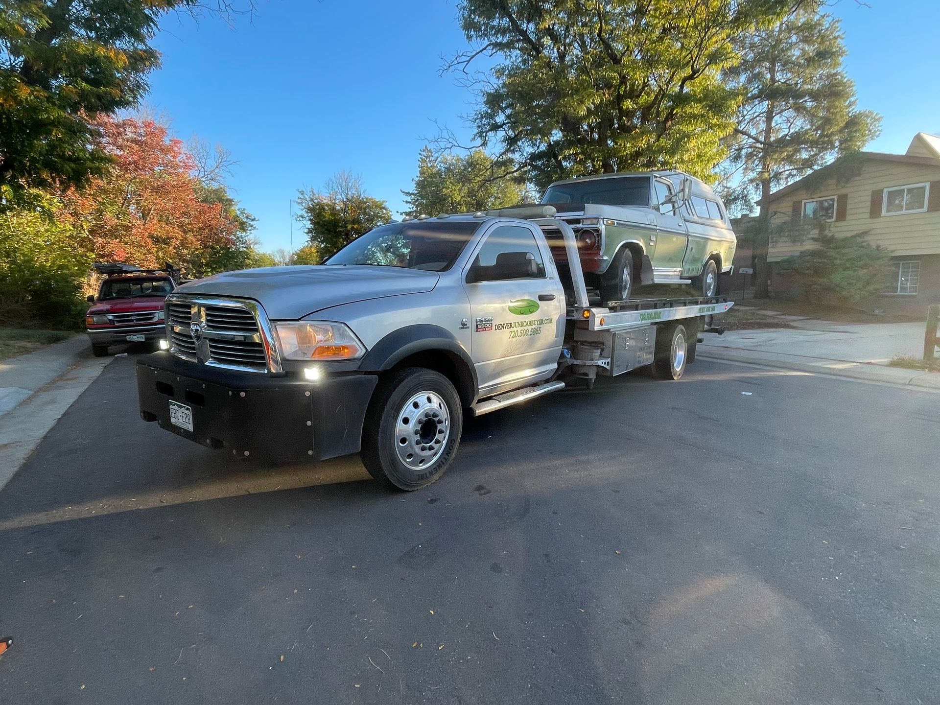 Tow truck carrying a silver pickup on a residential street with autumn trees and houses